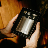 Person holding a silver flask set with initials 'AR' in a black box.
