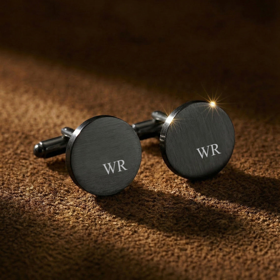 Black cufflinks with 'WR' initials on a brown textured surface